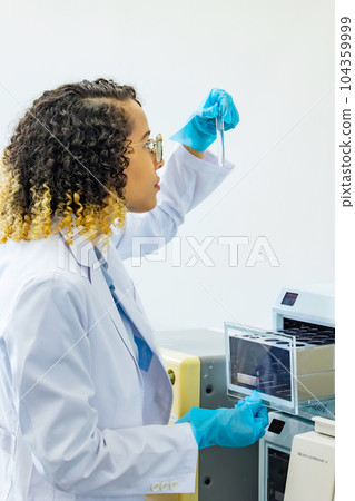 Foreign female scientist looking at test tube Foreign female scientist looking at test tube 104359999