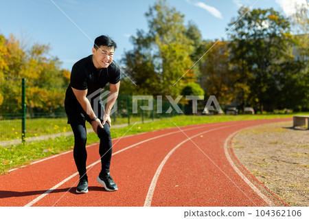 A runner injured his leg on a run in the afternoon, an Asian man has severe muscle spasm and pain in his leg during fitness and active exercise, a man in a tracksuit injured himself. 104362106