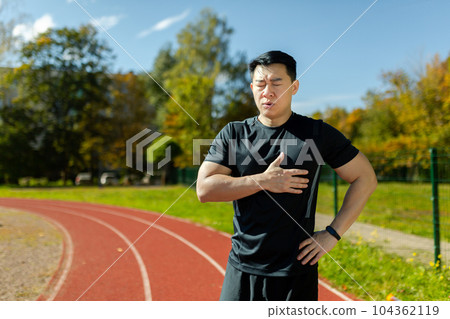 Asian tired and overworked while jogging and doing fitness active exercise, having severe chest pain, heart attack in sports stadium in man. Asian tired and overworked while jogging and doing fitness active exercise, having severe chest pain, heart attack in sports stadium in man. 104362119