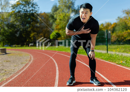 Heart attack while running and doing fitness and active exercise in stadium, asian mature man has severe chest pain. 104362120