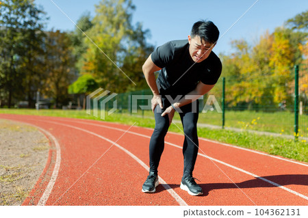 A runner injured his leg on a run in the afternoon, an Asian man has severe muscle spasm and pain in his leg during fitness and active exercise, a man in a tracksuit injured himself. 104362131