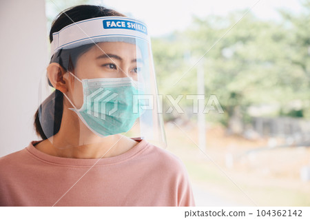 Asian woman wearing mask and face shield before going outside her room for prevent and protection covid-19 virus disease. 104362142