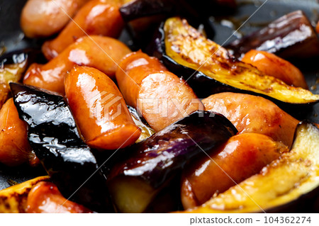 A cooking scene where eggplant and wiener sausage are fried in a frying pan. 104362274