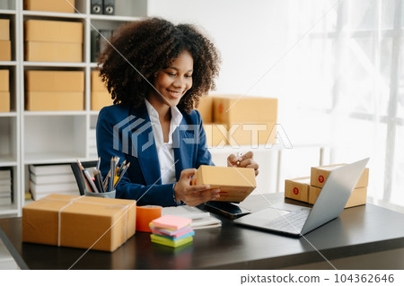 Startup small business SME, Entrepreneur owner African woman using smartphone or tablet taking receive and checking online purchase shopping order to preparing pack product box. . 104362646