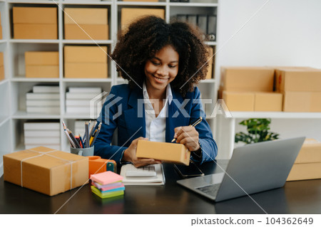 Startup small business SME, Entrepreneur owner African woman using smartphone or tablet taking receive and checking online purchase shopping order to preparing pack product box. . Startup small business SME, Entrepreneur owner African woman using smartphone or tablet taking receive and checking online purchase shopping order to preparing pack product box. . 104362649
