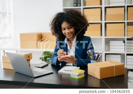 Startup small business SME, Entrepreneur owner African woman using smartphone or tablet taking receive and checking online purchase shopping order to preparing pack product box. . Startup small business SME, Entrepreneur owner African woman using smartphone or tablet taking receive and checking online purchase shopping order to preparing pack product box. . 104362650