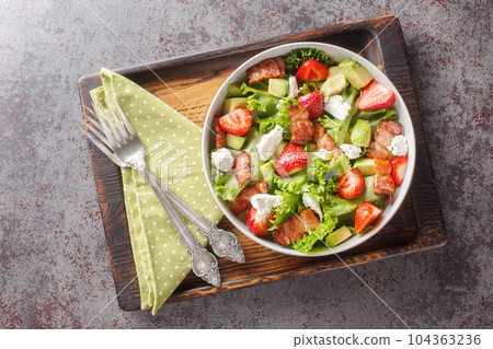 Homemade fresh salad of strawberries, avocado, bacon, lettuce, feta cheese close-up in a bowl. Horizontal top view 104363236
