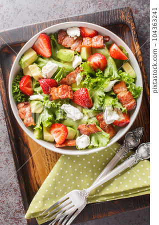 Delicious vitamin salad of strawberries, avocado, bacon, lettuce, feta cheese close-up in a bowl on the table. Vertical top view 104363241