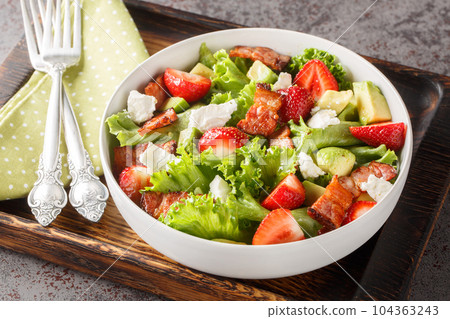 Salad with fresh strawberries, avocado, feta, bacon and lettuce on a wooden board close-up. Horizontal Salad with fresh strawberries, avocado, feta, bacon and lettuce on a wooden board close-up. Horizontal 104363243