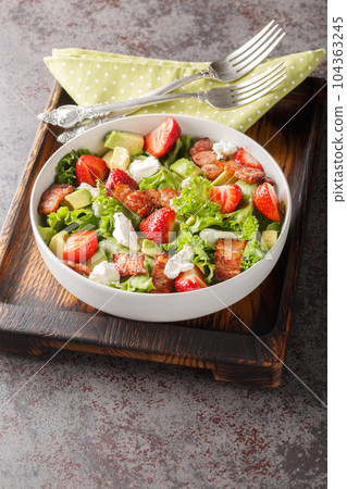 Summer salad of strawberries, avocado, bacon, lettuce, goat cheese close-up in a bowl. Vertical 104363245