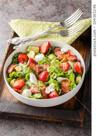 Delicious light salad of strawberries, avocado, bacon, lettuce, feta cheese close-up in a bowl. Vertical 104363246