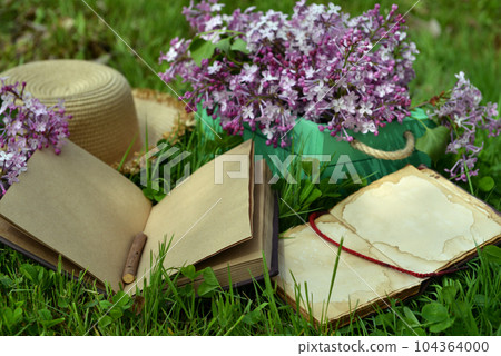 Vintage still life with open book or diary, hat and lilac flowers bouquet in the garden. Summer and spring season concept Vintage still life with open book or diary, hat and lilac flowers bouquet in the garden. Summer and spring season concept 104364000