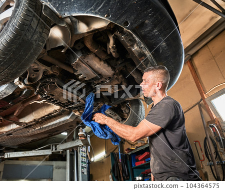 Repairman, worker repairing car, holding rag, wiping. Strong, hardworking man working in servicing center, mainteining automobiles. Concept of manual labor. 104364575