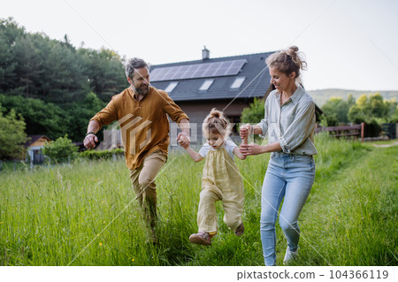 Family walking near their house with photovoltiacs panels on the roof. 104366119