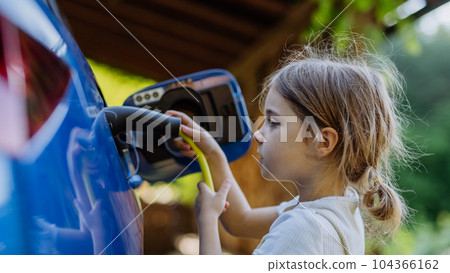 Little girl holding power supply cable and charging their electric car. 104366162