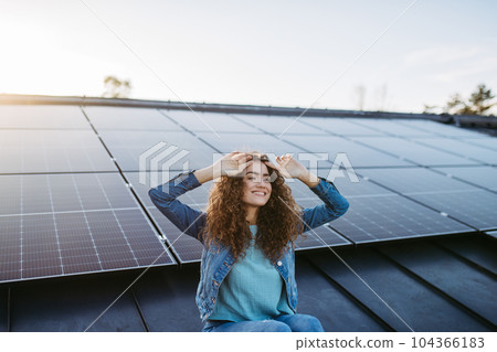 Portrait of young woman on roof with solar panels. 104366183