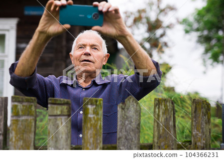 Old man with smartphone taking photographs outdoors 104366231