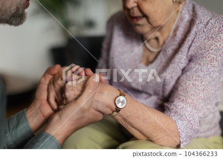 Close up of son holding hands of his senior mother, concept of healthcare and relationships. 104366233