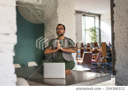 Young man sitting and meditating in his office. 104366312