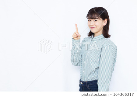 A woman in her thirties who raises her index finger in front of a white background 104366317