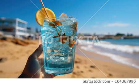 Blue refreshing cocktail at the beach in the woman hand on tropical beach background. Blue refreshing cocktail at the beach in the woman hand on tropical beach background. 104367990