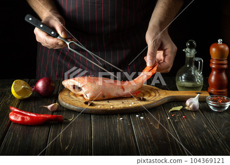 The chef prepares raw Sebastes fish. The concept of a delicious red fish lunch for a restaurant or hotel. Fork in the hand of the cook in the kitchen 104369121