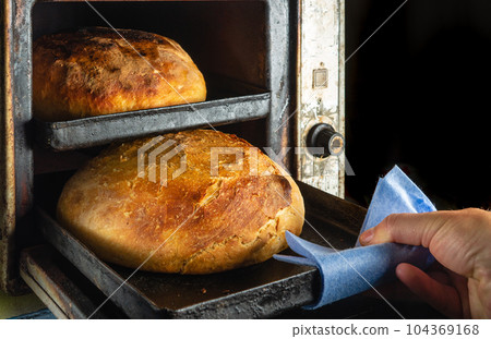 Baking Ukrainian bread at home. The baker takes out a tray with a loaf of bread from an old oven Baking Ukrainian bread at home. The baker takes out a tray with a loaf of bread from an old oven 104369168
