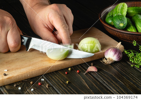 Slicing onions on a cutting board by the hands of a cook for preparing a vegetable salad. Menu for restaurant or hotel 104369174