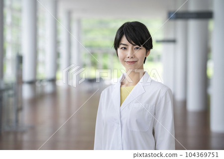 A woman in her 30s wearing a white coat looking at the camera portrait 104369751