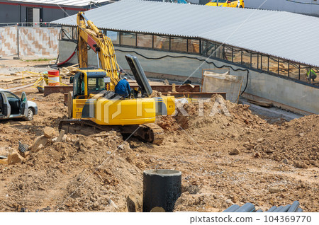 A man is repairing an excavator at a construction site. 104369770