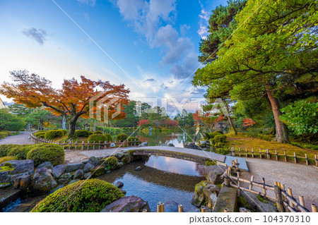 Landscape of Kotoji lanterns in Kenrokuen Kasumigaike Pond with beautiful autumn leaves and clear blue sky 104370310