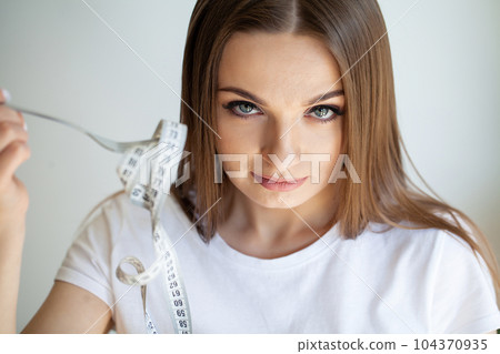 A woman holds a measuring tape as a symbol of weight loss A woman holds a measuring tape as a symbol of weight loss 104370935