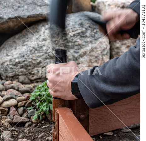 Actively driving a border stake with a rubber mallet to assemble a raised bed garden panel. 104371133