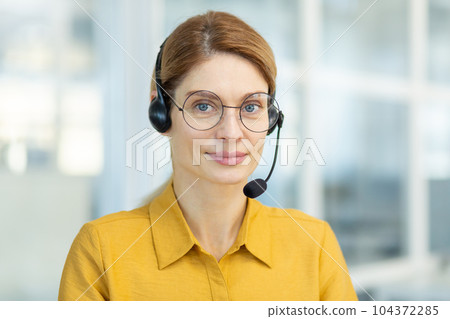 Portrait of successful smiling business woman with headset phone, mature experienced worker smiling and looking at camera, video call online meeting, online customer support service. 104372285