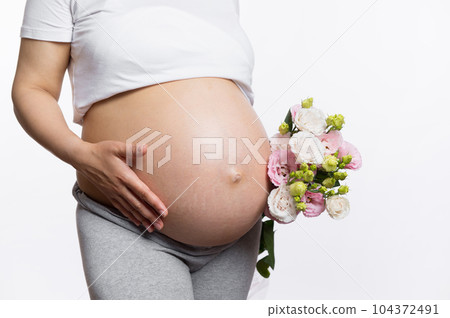 Close-up studio shot of a pregnant belly of gravid woman with a bouquet of flowers,isolated on white studio background. Healthy pregnancy, human fertility, gynecology and maternity concept. Eco banner Close-up studio shot of a pregnant belly of gravid woman with a bouquet of flowers,isolated on white studio background. Healthy pregnancy, human fertility, gynecology and maternity concept. Eco banner 104372491