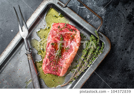 Marinated Raw striploin, New york steak with olive oil, thyme and pepper. Black background. Top view 104372839