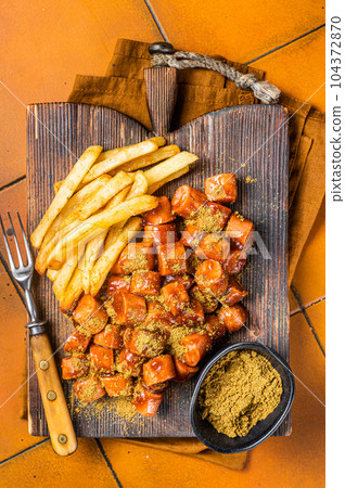 Curried sausage currywurst meal, curry wurst with french fry served on a wooden board. Orange background. Top view 104372870