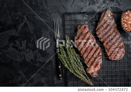 Grilled denver beef meat steak on a rack. Black background. Top view. Copy space Grilled denver beef meat steak on a rack. Black background. Top view. Copy space 104372872
