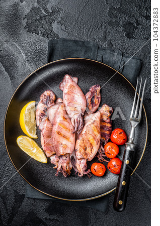 Seafood diner with grilled squid, calamary in a plate. Black background. Top view 104372883