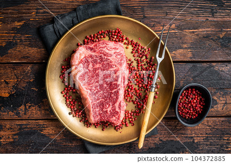 Raw Wagyu striploin, New york steak on a plate with pink peppper. Wooden background. Top view 104372885