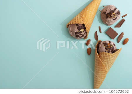Chocolate ice cream in a waffle cone, blue background, flat lay, top view, copy space. Summer cooling desserts Chocolate ice cream in a waffle cone, blue background, flat lay, top view, copy space. Summer cooling desserts 104372992