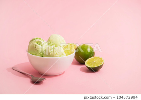 Ice cream with lime flavor and slices of fresh lime in a white bowl, pink background, copy space. Summer cooling desserts, 104372994
