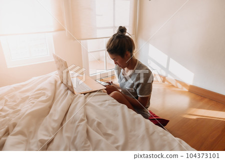 Woman working online business in her bedroom. Woman working online business in her bedroom. 104373101