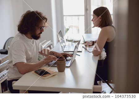 Married couple freelancers sit at table in living room with laptops and working from home office Married couple freelancers sit at table in living room with laptops and working from home office 104373530