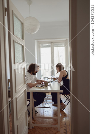 Married couple freelancers sit at table in living room with laptops and working from home office Married couple freelancers sit at table in living room with laptops and working from home office 104373532