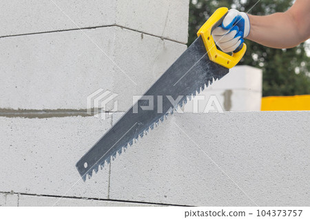 Worker sawing a gas block at a construction site. Worker sawing a gas block at a construction site. 104373757