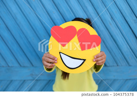 A human holds a romantic emoticon in love with eyes in the shape of hearts on a blue background 104375378
