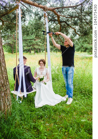Videographer shoots a film with the newlyweds on a rope swing in a pine forest 104375430