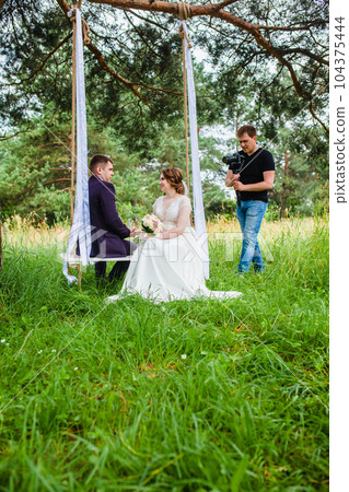 Videographer shoots a film with the newlyweds on a rope swing in a pine forest Videographer shoots a film with the newlyweds on a rope swing in a pine forest 104375444