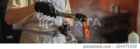 Close-up view of chef in uniform stir frying bacon in pan for cooking dish in restaurant kitchen 104375520
